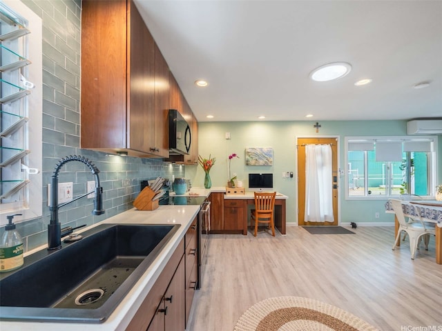 kitchen with a sink, a wall mounted AC, brown cabinetry, black microwave, and electric range