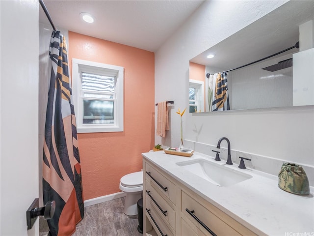 full bathroom featuring a textured wall, baseboards, toilet, wood finished floors, and vanity