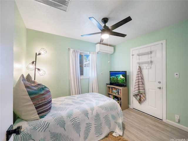 bedroom featuring ceiling fan, light wood finished floors, baseboards, visible vents, and a wall unit AC