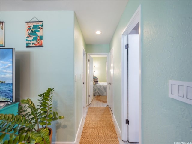 hallway with recessed lighting, a textured wall, light colored carpet, and baseboards
