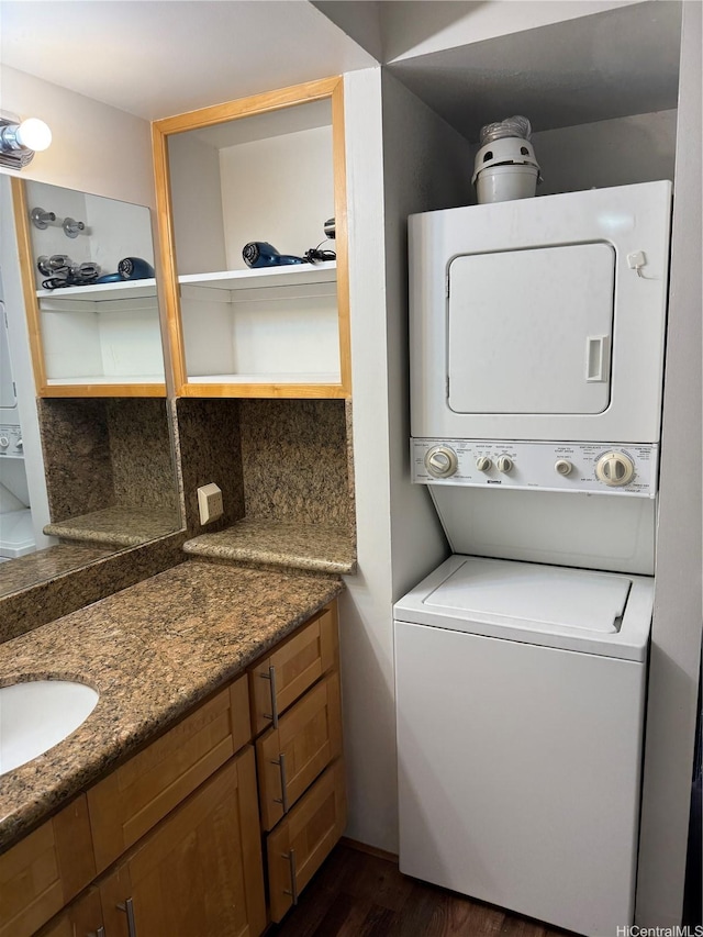 laundry room featuring stacked washer and dryer, laundry area, dark wood-style flooring, and a sink