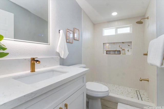 bathroom with toilet, a tile shower, and vanity