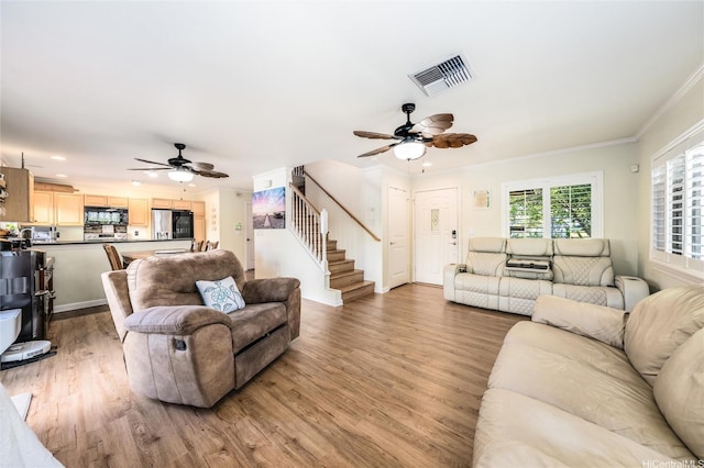 living room featuring crown molding, stairway, visible vents, ceiling fan, and light wood-style floors