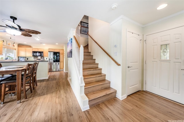 foyer with crown molding, light wood-style flooring, ceiling fan, and stairs
