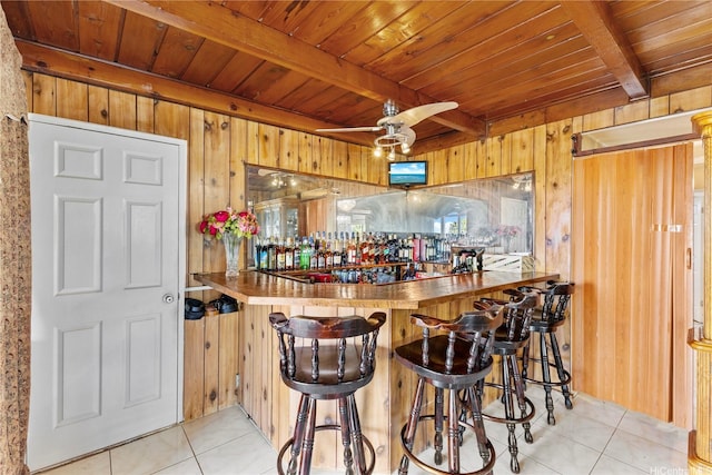 bar featuring light tile patterned floors, beamed ceiling, wood walls, a bar, and wooden ceiling