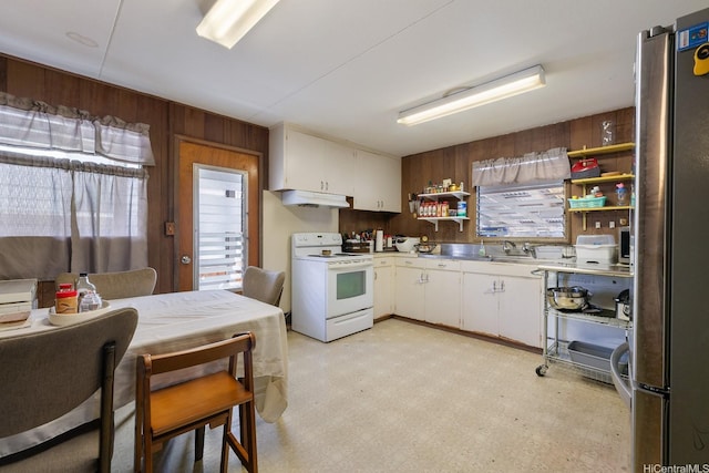 kitchen with electric stove, wood walls, white cabinetry, and freestanding refrigerator