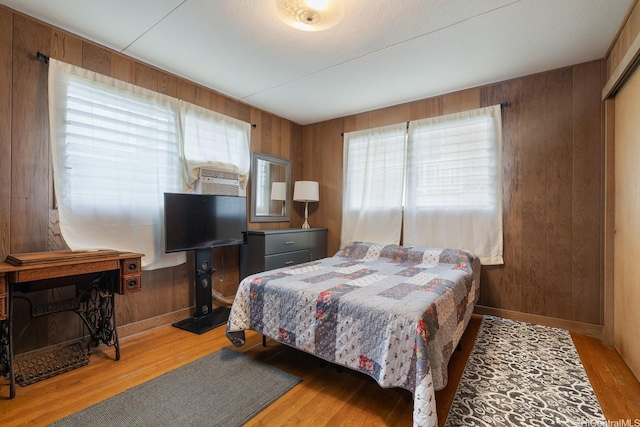 bedroom featuring wood walls, light wood-style floors, and multiple windows