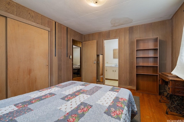 bedroom featuring a sink, a closet, ensuite bath, wood walls, and wood finished floors