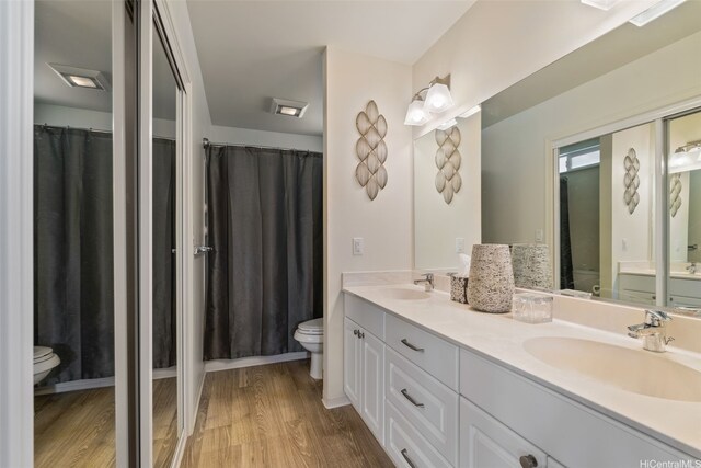 bathroom with a sink, double vanity, toilet, and wood finished floors