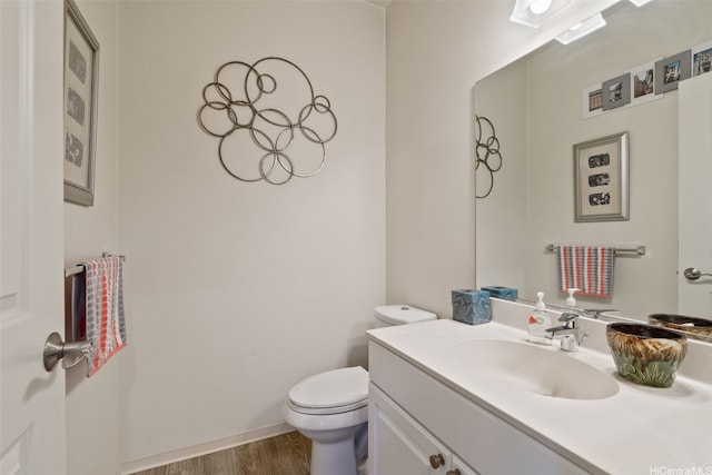 half bathroom with vanity, baseboards, wood finished floors, and toilet