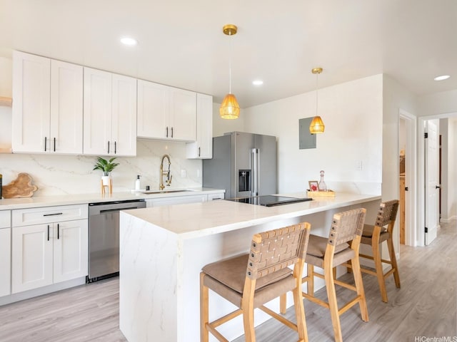 kitchen with white cabinets, stainless steel appliances, light wood finished floors, and a sink