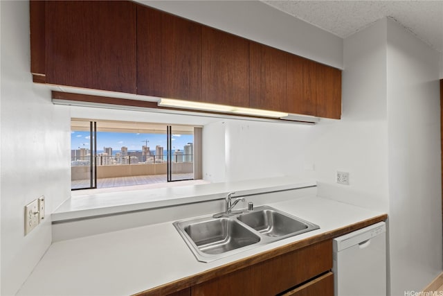 kitchen with a textured ceiling, white dishwasher, light countertops, a sink, and a view of city