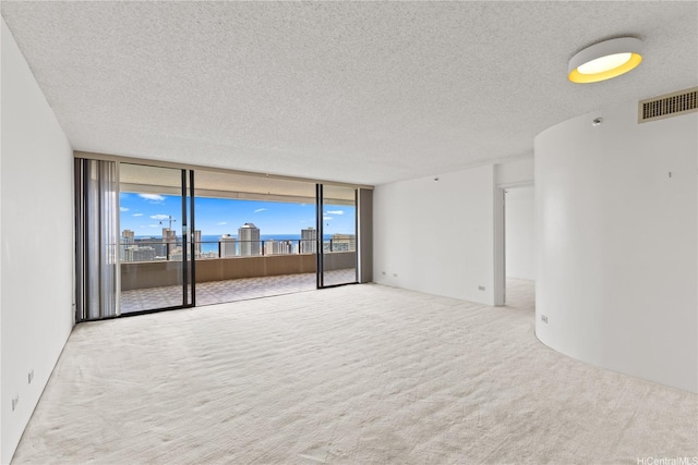carpeted spare room with a textured ceiling, visible vents, and floor to ceiling windows