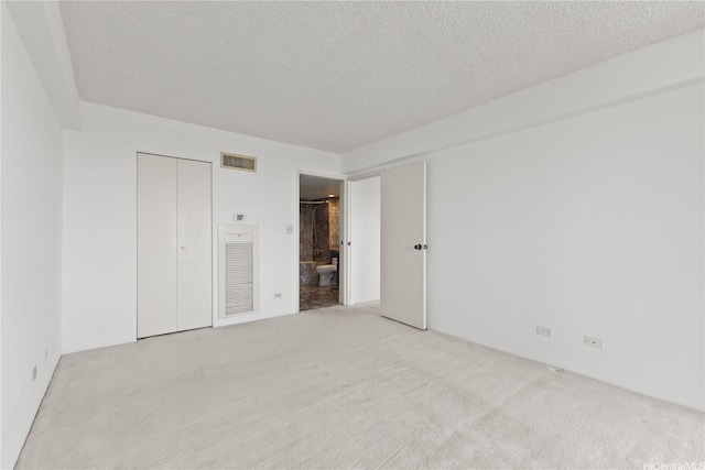 unfurnished bedroom with carpet flooring, a textured ceiling, visible vents, and ensuite bath