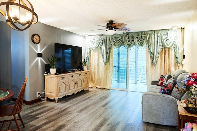 living area featuring a textured ceiling, wood finished floors, and ceiling fan with notable chandelier