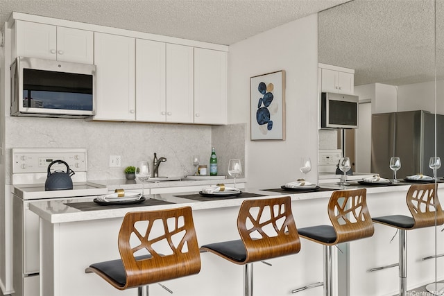 2211 Ala Wai Blvd Unit 2015, Honolulu, HI 96815 - kitchen featuring decorative backsplash, a kitchen breakfast bar, a textured ceiling, white cabinets, and appliances with stainless steel finishes