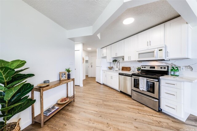 1031 Maunaihi Pl Unit 802, Honolulu, HI 96822 - kitchen featuring appliances with stainless steel finishes, a sink, light wood-style floors, white cabinetry, and a textured ceiling