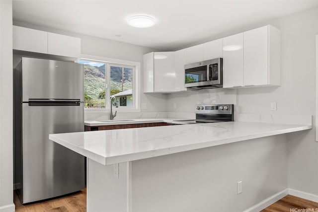 kitchen featuring appliances with stainless steel finishes, a sink, a peninsula, white cabinetry, and light wood-type flooring