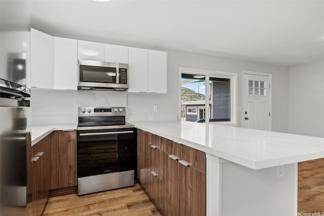 kitchen with appliances with stainless steel finishes, modern cabinets, light wood finished floors, and a peninsula