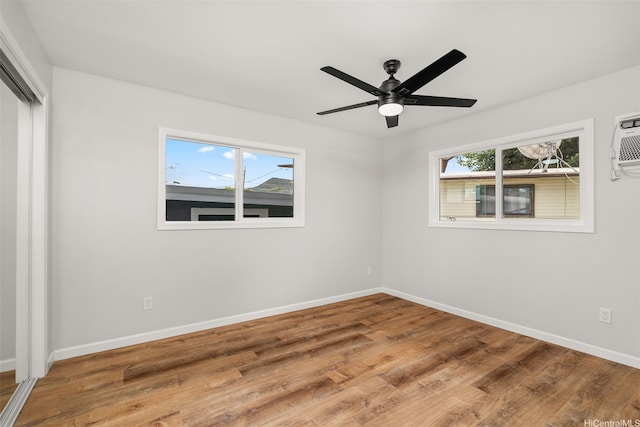 unfurnished bedroom with ceiling fan, a wall mounted air conditioner, baseboards, wood finished floors, and a closet