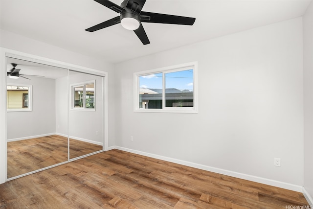 unfurnished bedroom featuring baseboards, a ceiling fan, wood finished floors, and a closet
