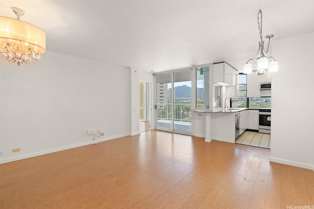 unfurnished living room featuring an inviting chandelier, a mountain view, a sink, baseboards, and light wood-type flooring