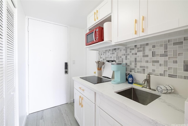 kitchen featuring a sink, tasteful backsplash, black electric stovetop, light stone counters, and white cabinetry