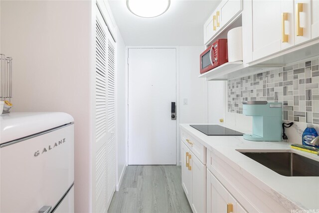kitchen featuring light wood-style flooring, white cabinetry, backsplash, light countertops, and black electric stovetop