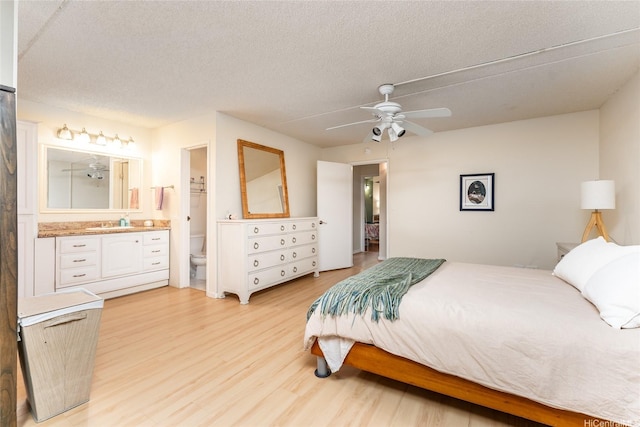 bedroom with ensuite bath, a textured ceiling, light wood-style flooring, and a sink