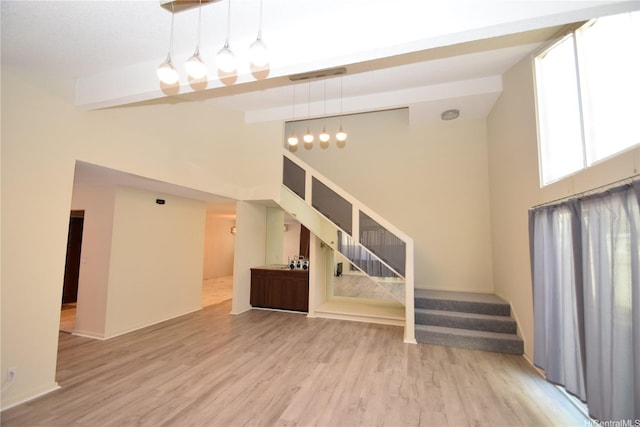 unfurnished living room featuring beam ceiling, wood finished floors, high vaulted ceiling, stairway, and baseboards