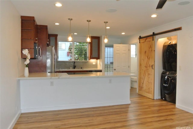 kitchen with backsplash, stacked washer / drying machine, light countertops, freestanding refrigerator, and a peninsula