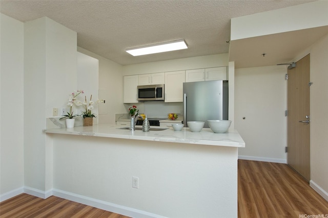 1133 Waimanu St Unit 201, Honolulu, HI 96814 - kitchen with a sink, stainless steel appliances, white cabinetry, a peninsula, and wood finished floors