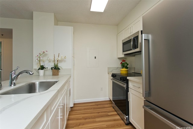1133 Waimanu St Unit 201, Honolulu, HI 96814 - kitchen featuring white cabinetry, a textured ceiling, a sink, light wood-style flooring, and appliances with stainless steel finishes
