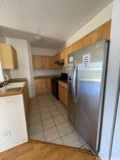 kitchen featuring stainless steel refrigerator with ice dispenser, a textured ceiling, a sink, black gas range, and under cabinet range hood
