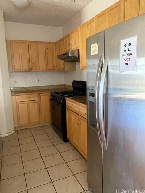 kitchen featuring stainless steel fridge, light tile patterned floors, black gas range oven, and under cabinet range hood