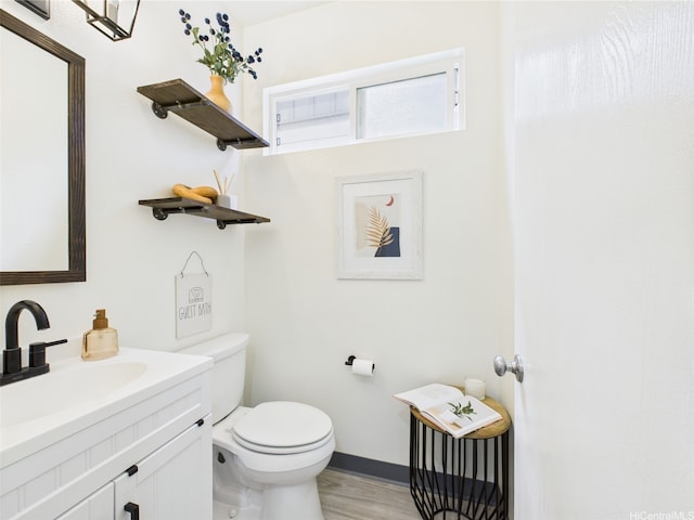 half bathroom featuring toilet, vanity, wood finished floors, and baseboards