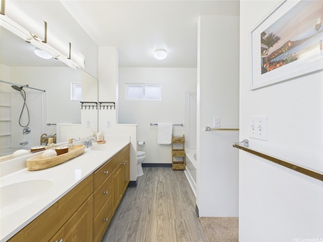 bathroom with tub / shower combination, toilet, wood finished floors, and double vanity