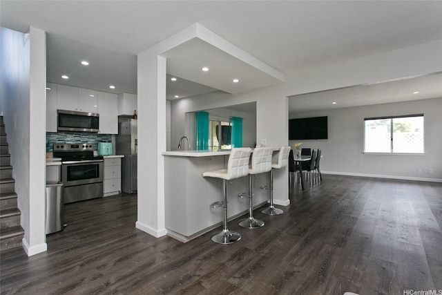 kitchen with light countertops, stainless steel appliances, a kitchen bar, dark wood-style floors, and modern cabinets