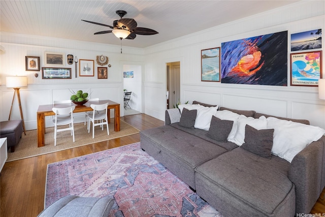 living area with crown molding, a ceiling fan, a decorative wall, and wood finished floors