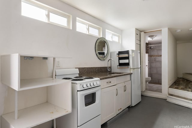 kitchen with white appliances, a sink, white cabinets, finished concrete flooring, and dark stone counters
