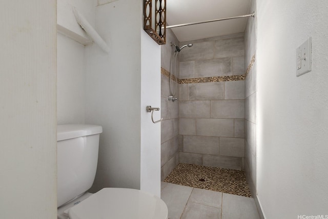 bathroom featuring toilet, a tile shower, and tile patterned floors