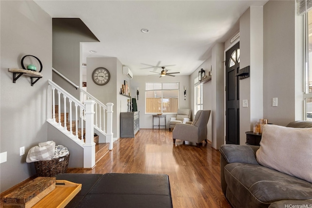 living area with ceiling fan, an AC wall unit, stairs, baseboards, and wood finished floors