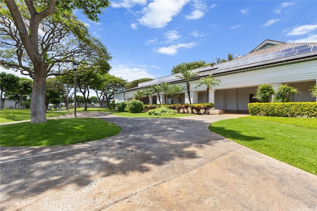 view of front facade featuring curved driveway, solar panels, and a front yard