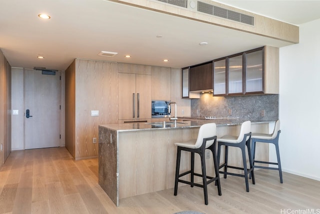 1000 Auahi St Unit 1404, Honolulu, HI 96814 - kitchen with light stone countertops, light wood-style flooring, a peninsula, decorative backsplash, and visible vents