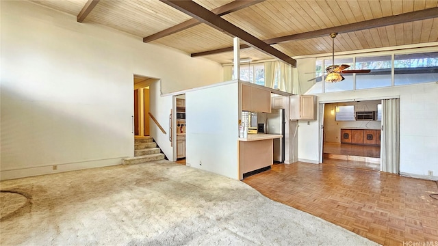 unfurnished living room with a healthy amount of sunlight, ceiling fan, beam ceiling, and a high ceiling