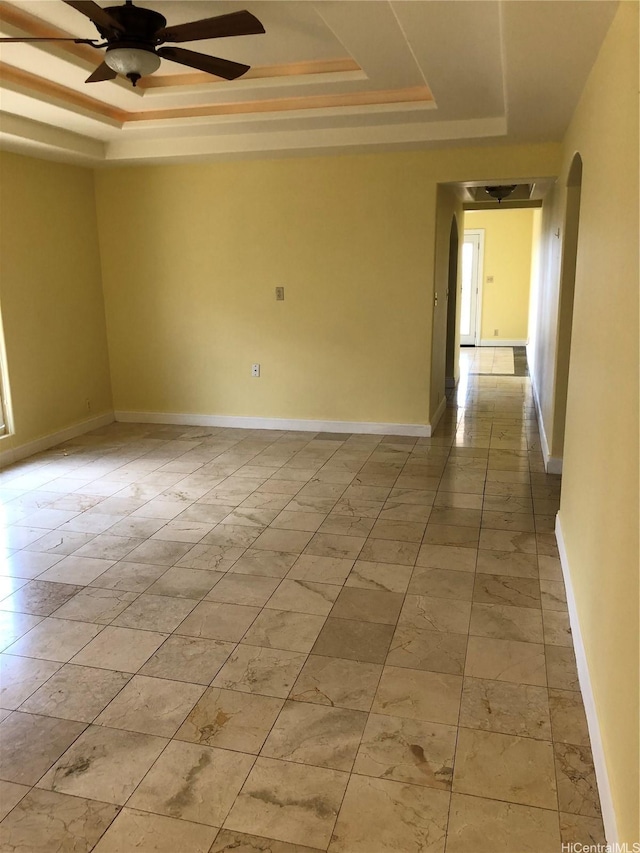 empty room with baseboards, a ceiling fan, arched walkways, and a tray ceiling