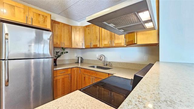 kitchen with a sink, freestanding refrigerator, brown cabinetry, ventilation hood, and stove