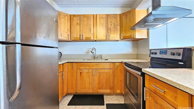 kitchen with wall chimney range hood, brown cabinets, appliances with stainless steel finishes, and a sink
