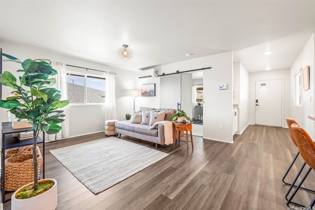 living area with wood finished floors, a barn door, baseboards, and a wall unit AC