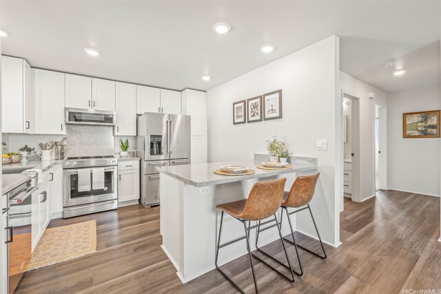 kitchen with a peninsula, stainless steel appliances, wood finished floors, white cabinetry, and a kitchen bar
